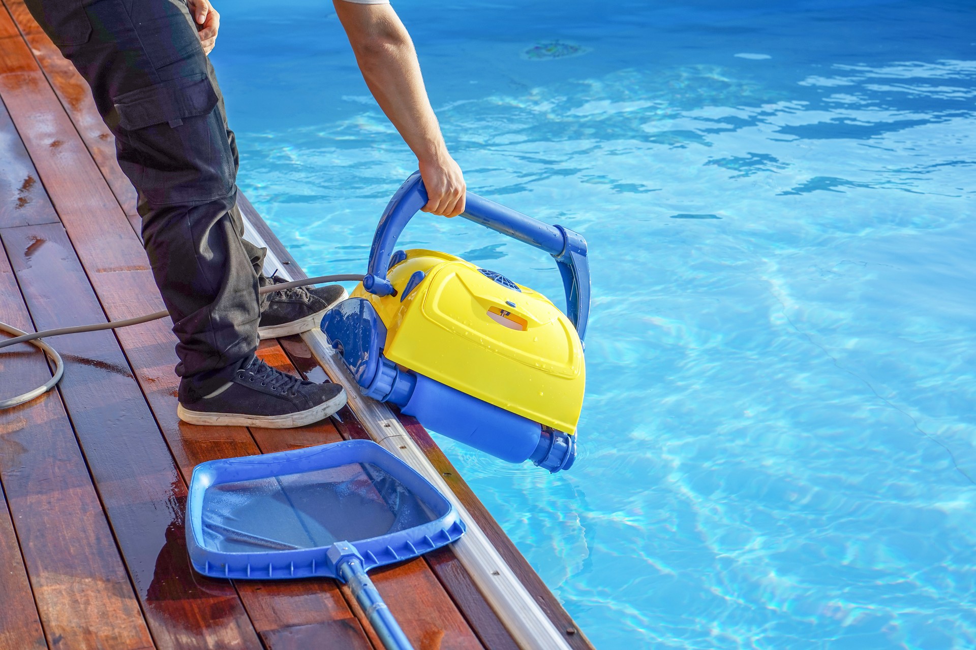 Hotel staff worker cleaning the pool. A pool cleaner holds a robot cleaner.